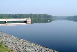 Photograph of Cane Creek Reservoir showing rocky shore, lake, and distant trees in the mist