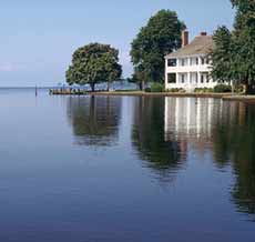 Photograph of house and trees reflecting in a still body of water.