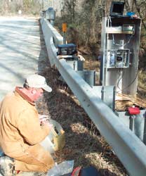 Photograph of a USGS scientist servicing hydrologic instrumentation at a roadside streamgaging station.