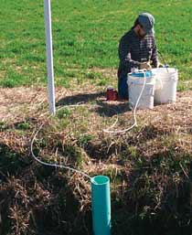 Photograph of a USGS scientist collecting water-quality samples from a tile drain beneath cropland.