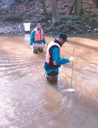 Photograph of two USGS scientists collecting a streamwater sample in the Eno River.