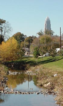 Photograph of a streambed near the city of Charlotte with the  Charlotte skyline in the background.